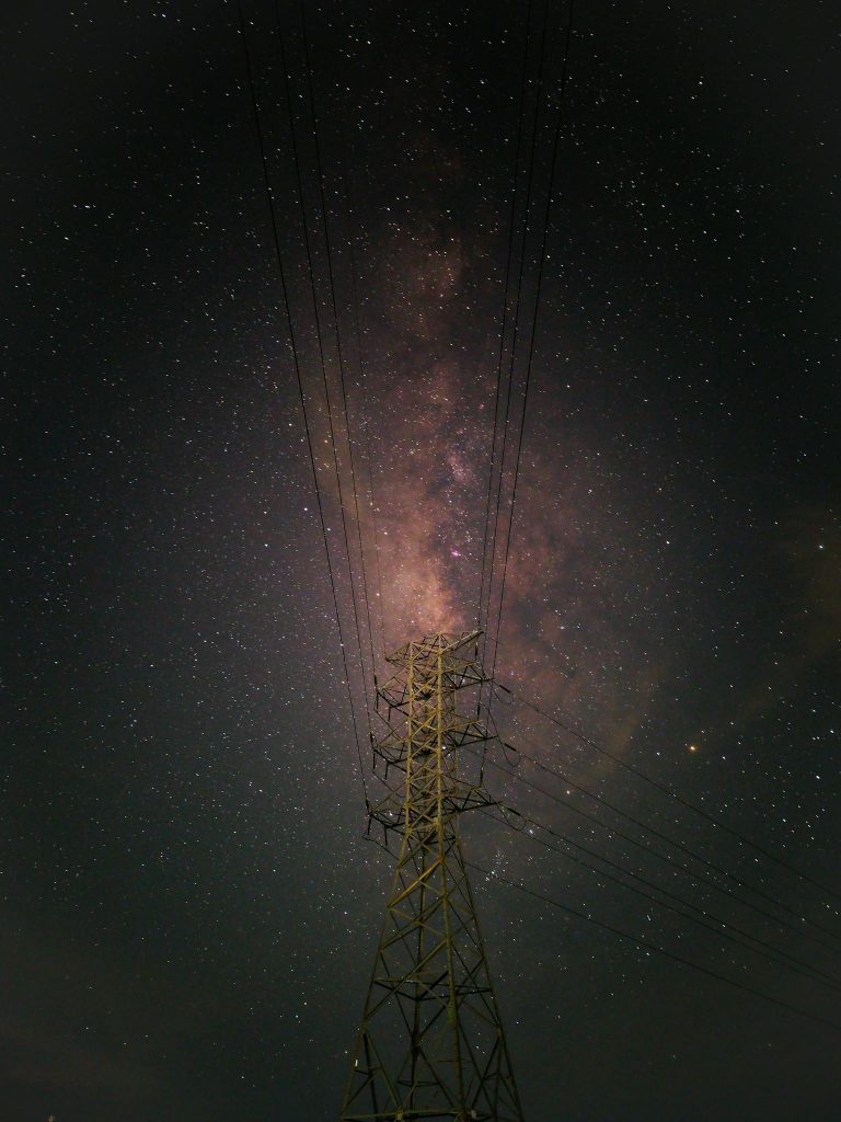 A breathtaking view of the Milky Way galaxy shining brightly over a power transmission tower at night.
